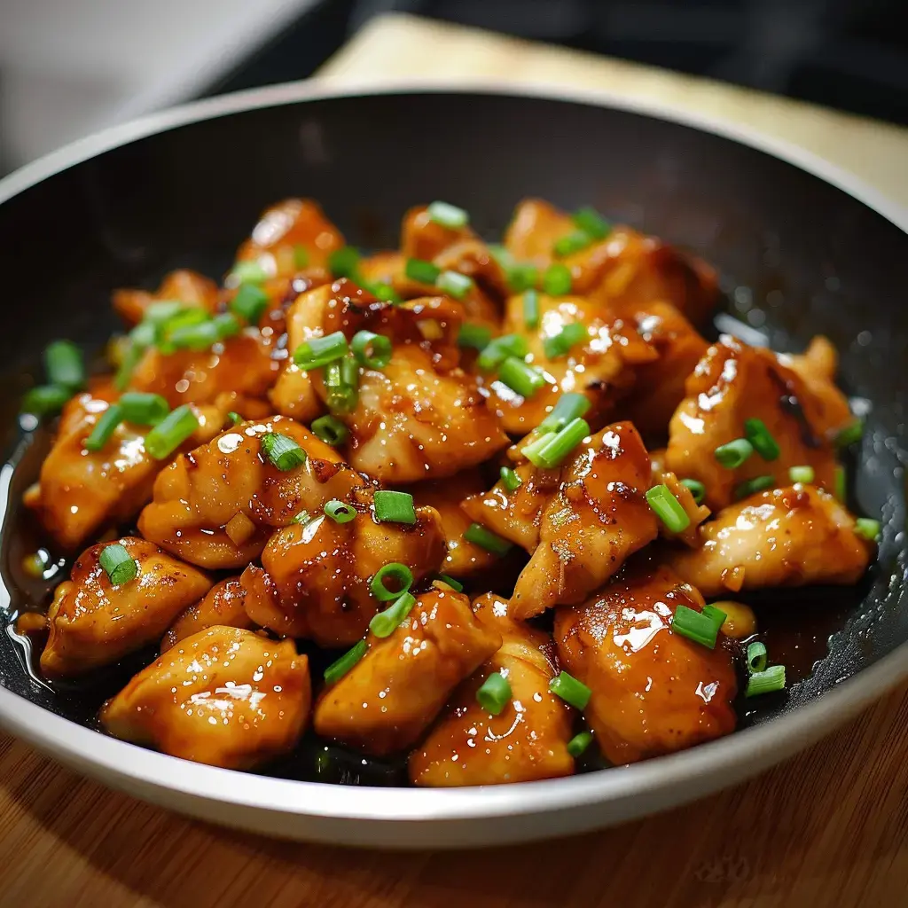 Un bol noir rempli de poulet caramélisé nappé de sauce sucrée avec des herbes fraîches.