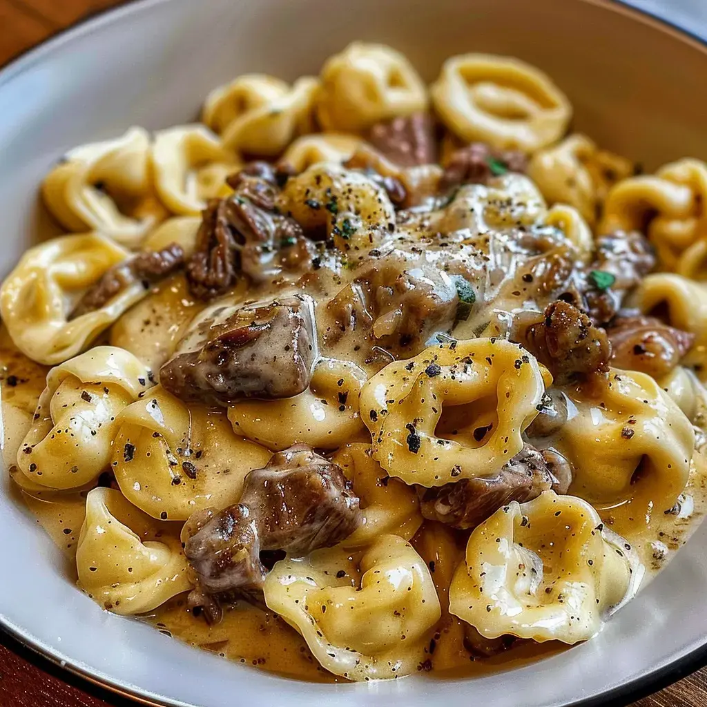 Un bol rempli de tortellinis nappés de sauce crémeuse au fromage, accompagnés de viande et épices.