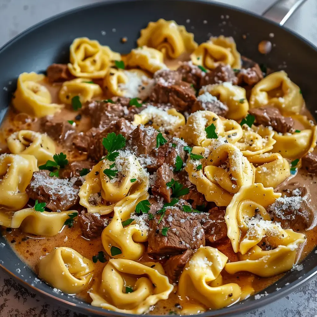 Un bol gourmand de tortellini en sauce crémeuse, garni de bœuf tendre et de parmesan avec une touche de persil.