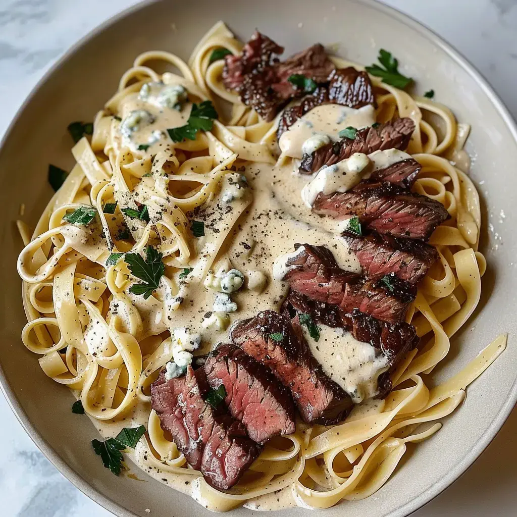 Assiette de fettuccine recouverte de tranches de bœuf et de sauce crémeuse décorée de persil et fromage bleu.