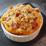 Un plat de purée de courge onctueuse avec des morceaux de lardons, recouvert d'une épaisse couche de chapelure dorée et croustillante.