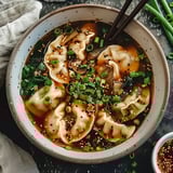 Un bol rempli de raviolis, oignons verts, graines de sésame et légumes dans un bouillon fumant.