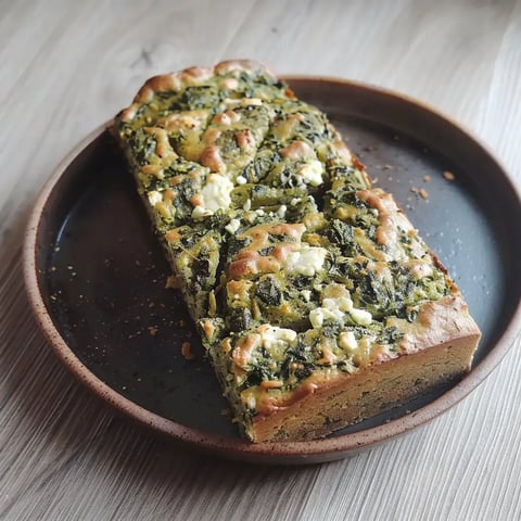 Un cake aux épinards et feta décoré élégamment sur une assiette rustique.